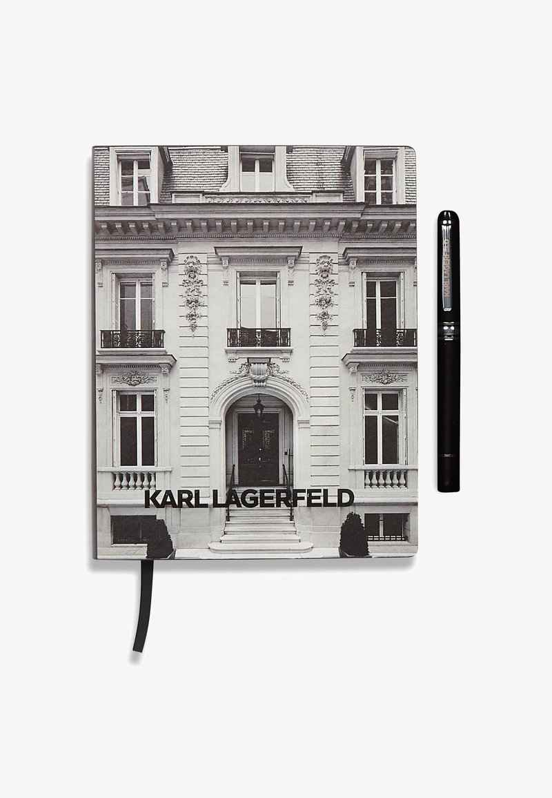 Crno-bijeli notes s fotografijom fasade imanja. Tekst glasi "KARL LAGERFELD." Uz njega se nalazi crna olovka.