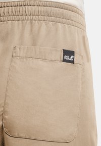 Shorts kaki avec une poche arrière ornée d'une étiquette noire affichant le logo "Jack Wolfskin". Tissu lisse à texture unie avec une ceinture élastique.
