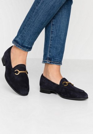 Marineblå mokkasiner i ruskind med gyldent hestebidsdetalje båret med opsmøgede blå skinny jeans på grå gulv.
