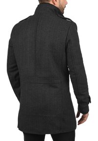 Tmavě šedý kabát s rybí kostí vzoru, vysokým límcem, viditelným šitím a knoflíkovými detaily na rukávech. Střih na míru, střední délka.