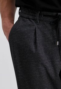 Grijze gestreepte broek van een gestructureerde stof. Heeft een elastische tailleband met een trekkoord en zijzakken.