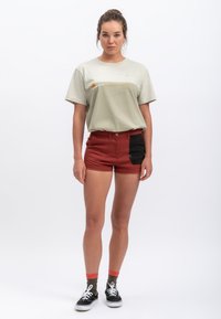 Lichtgroene katoenen T-shirt met een horizontaal kleurblokdetail, gecombineerd met rode denim shorts met een zwarte zijzak en stiksels.