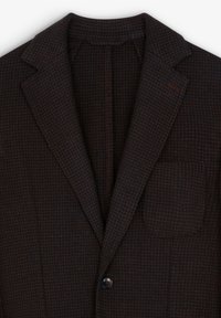 Blazer de patrón de espiga marrón con solapas de muesca, cierre de un solo botón y bolsillo en el pecho. Tejido texturizado con costuras visibles que acentuán el diseño.