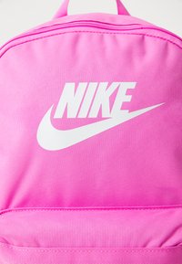 Roze stoffen rugzak met wit Nike-logo. Het ontwerp heeft een textuurmateriaal en een bovenrits voor sluiting. Eenvoudige, gestroomlijnde vorm.