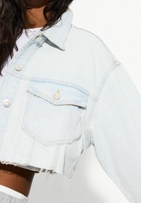 Ljus tvättad denimjacka i cropped-modell med spetsig krage, två framfickor och slitna kanter. Har silverfärgade knappar och mjuk textur.