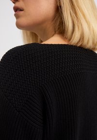 Czarny sweter z dzianiny z teksturowanym wykończeniem na ramionach i prążkowanymi detalami. Materiał ma miękki, gruby wygląd i luźny krój.