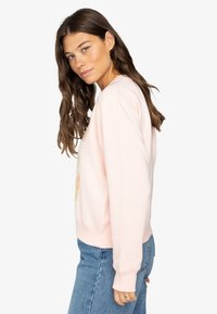 Hellrosa Sweatshirt mit Rundhalsausschnitt und gerippten Bündchen, mit einem bunten Grafikdruck auf der Vorderseite, kombiniert mit blauen Jeans.