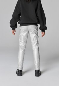 Silver metalliska slim fit byxor med sidofickor och bakfickor, kombinerat med en svart oversized sweatshirt och kraftiga svarta stövlar.