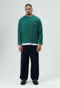 Turquoise fleece sweater met een ronde hals, gecombineerd met brede donkere jeans en zwarte veter schoenen. Gegarandeerde zachte, gestructureerde stof.