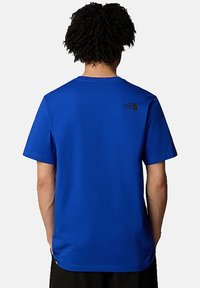 Camiseta de manga corta azul en una tela suave, con un pequeño logo negro en la parte superior de la espalda, con un clásico escote redondo y ajuste relajado.