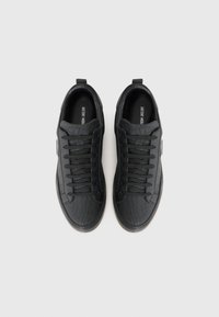 Black sneakers with textured leather upper, flat laces, and round toe. Minimalist design with subtle branding on the insole. Rubber outsole.
