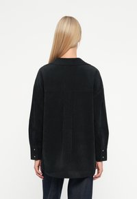 Czarna kurtka koszulowa z korduroy z kołnierzem ze szczeliną, długimi rękawami i guzikami przy mankietach; posiada szczegół szwu na plecach.