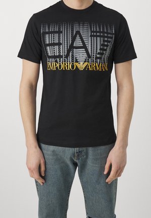 Schwarzes Baumwoll-T-Shirt mit einem auffälligen grauen und gelben Grafikdesign "EA7 EMPORIO ARMANI", das eine Mischung aus fetten und dünnen Buchstaben zeigt.