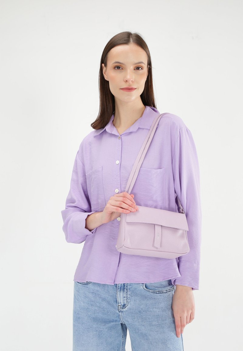 Lyse lilla langærmet skjorte med knapdetaljer og to lommer, parret med en lille lyse lilla læderhåndtaske, båret crossbody.