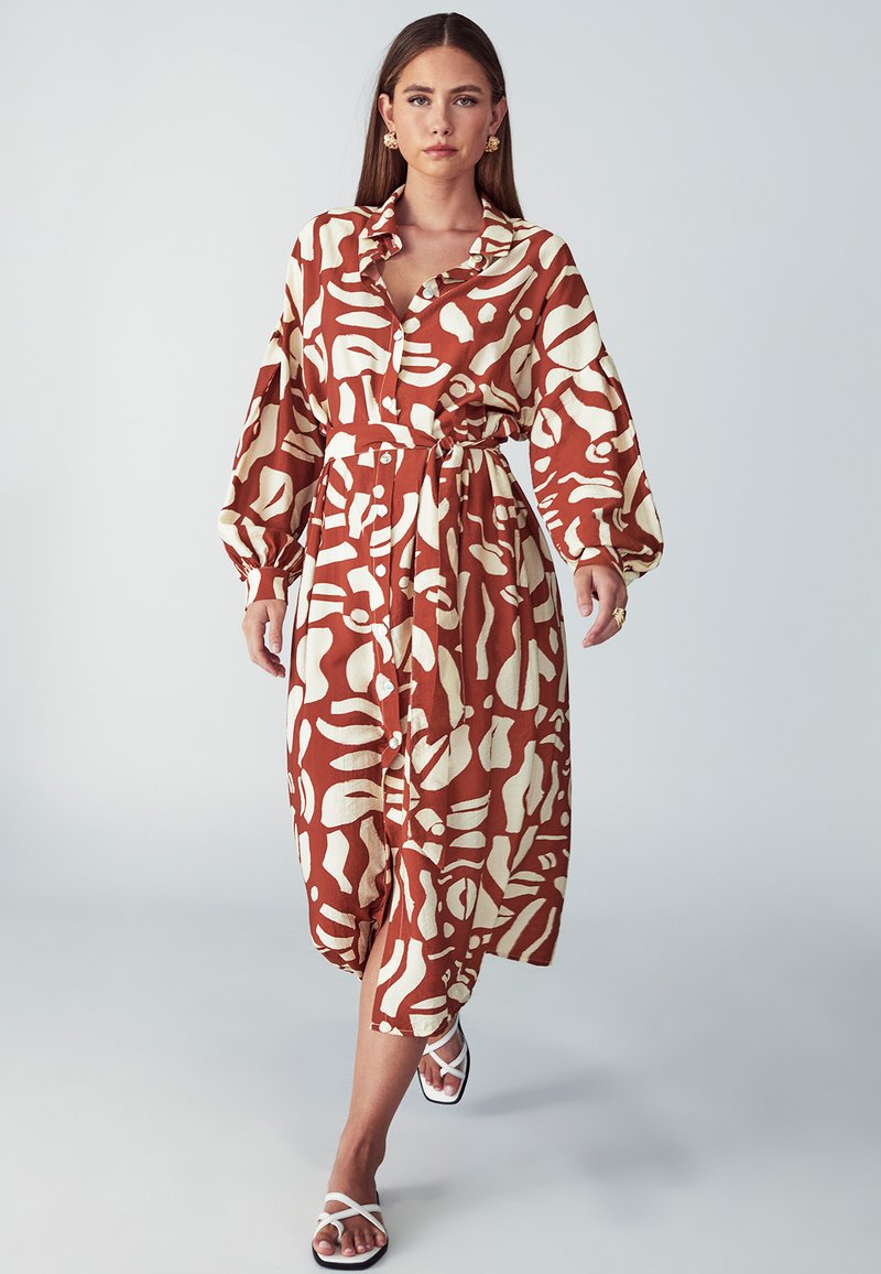 Tiskana haljina u boji rđe i kreme, s kopčanjem na gumbe, dugim rukavima i pojasom u struku; izrađena od lagane, teksturirane tkanine.