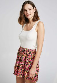 Débardeur blanc à bords festonnés associé à une jupe noire avec des motifs floraux roses, orange et jaunes, et une taille élastique.