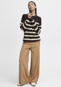 Maglione a strisce marroni e crema con maniche lunghe, abbinato a pantaloni larghi color beige e sneakers bianche. Tessuto liscio, vestibilità comoda.