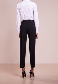 Bílá košile s dlouhým rukávem v kombinaci s černými oblečenými kalhotami. Kalhoty mají slim fit střih a mírný lesk, doplněné černými špičatými podpatky.