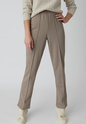 Pantalones beige de corte relajado, con un acabado texturizado, detalles de costuras verticales y una cinturilla elástica, combinados con zapatillas de tono claro.