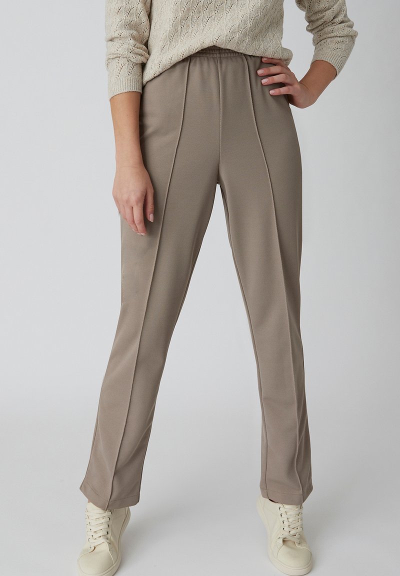 Beige broek met een relaxte pasvorm, voorzien van een gestructureerde afwerking, verticale naden en een elastische tailleband, gecombineerd met lichtgekleurde sneakers.