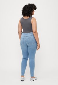 Bodysuit sin mangas gris combinado con jeans ajustados de color azul claro. Los jeans tienen una cintura alta, bolsillos traseros y una textura de denim suave. Unos zapatos planos plateados completan el look.