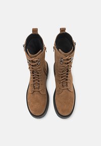 Bottines en daim marron avec bouts ronds, lacets sur le devant, fermetures éclair sur les côtés et semelles en caoutchouc texturé. Comprend des accents cousus et un col rembourré.