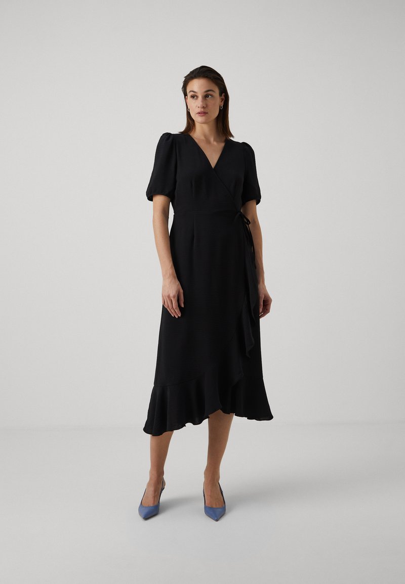Black wrap dress with short puff sleeves, a flared hem, and a tie at the waist. Smooth fabric with a subtle texture. Paired with light blue heels.
