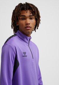 Lila Sporttop mit Viertelreißverschluss und strukturiertem Finish sowie schwarzen Akzenten. Verfügt über ein Logo auf der Brust und ein kontrastierendes Schulterdesign.