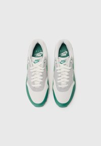 Sivé a zelené tenisky Nike Air Max s vrchom z meshu a syntetických materiálov, okrúhlym špičkou, bielymi šnúrkami a výrazným logom na jazyku.