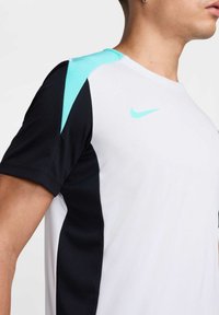 Camisa deportiva de Nike con un cuerpo blanco, mangas negras y un acento de turquesa claro en el hombro. Fabricada con tejido ligero y transpirable.