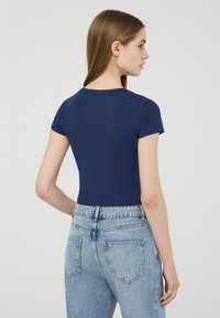 T-shirt aderente a maniche corte di colore blu navy realizzata in cotone morbido, abbinato a jeans in denim chiaro a vita alta con due tasche posteriori.