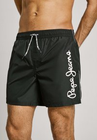 Svart svømmeshorts med elastisk midje og snøring, hvit merkevare langs siden, og et glatt, lett materiale.