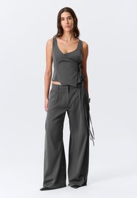 Ensemble à rayures grises comprenant un haut portefeuille sans manches avec liens latéraux et un pantalon à jambes larges. Tissu lisse avec une coupe ajustée.