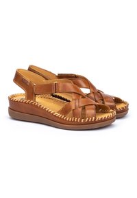 Sandalias de cuero marrón con tiras cruzadas y punta abierta. Presenta una plantilla acolchada y detalles trenzados a lo largo de los bordes, con un tacón cuña bajo.
