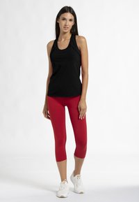 Zwart mouwloos sporttanktop gecombineerd met rode leggings en witte sneakers. Het tanktop heeft een ronde halslijn en een fitted ontwerp.