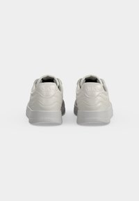 Paire de baskets blanc cassé vues de dos avec semelles surélevées et le nom de la marque ARKK embossé sur la zone du talon.