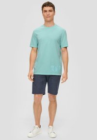 Lichtblauwe t-shirt met korte mouwen en ronde hals, voorzien van printdetails. Gecombineerd met marineblauwe gestreepte shorts en witte low-top sneakers.