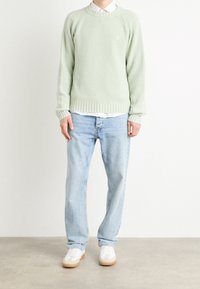 Maglione ribbed verde chiaro con collo a giro, abbinato a jeans azzurri e sneakers bianche. Presenta maniche lunghe e tessuto testurizzato.