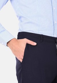 Pantaloni blu con un design snello, dotati di una tasca laterale e una texture morbida. Abbinati a una camicia a righe blu chiaro.