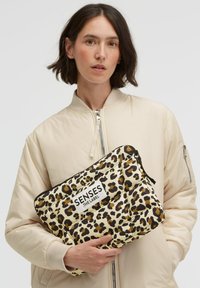 Gesteppte Clutch mit Leopardenmuster und weißem Logo-Patch, ausgestattet mit einem Reißverschluss. Das Material ist weich mit einer glänzenden Oberfläche, vorwiegend beige und braun.