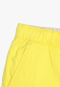 Žluté kraťasy s elastickým pasem a nařasenou texturou. Mají postranní švy a jsou vyrobeny z odolné směsi bavlny.