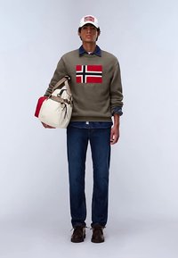 Pull vert avec un motif du drapeau norvégien, chemise en denim bleu, jean foncé, chaussures marron et sac crème avec des accents rouges. Casquette blanche.