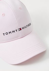 Casquette en coton rose avec visière incurvée. Présente un texte brodé "TOMMY HILFIGER" avec des accents de logo rouge et bleu à l'avant. Fini en tissu texturé.