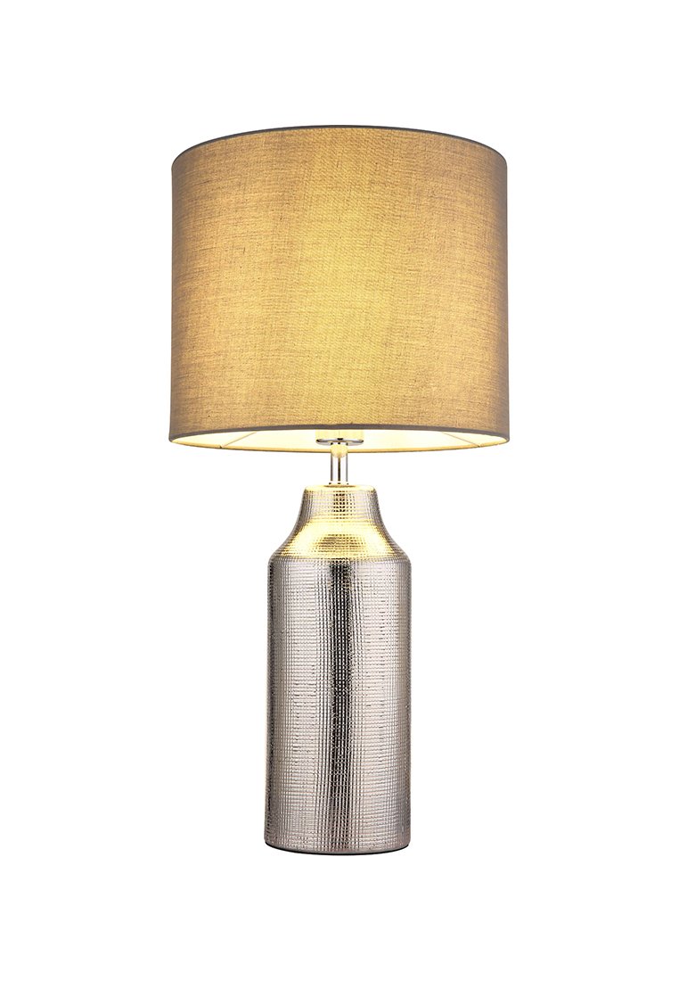 Stolní lampa s texturovaným stříbrným podstavcem a béžovým textilním stínidlem. Podstavec má cylindrický tvar a jemné vzorové detaily.