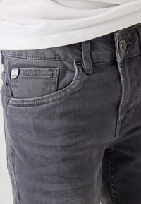 Grijze denim jeans hebben vijf zakken, een knoopsluiting en een lichte vervaging voor textuur. De stof is zacht met een gladde afwerking.