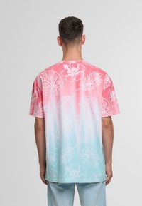 Short-sleeve t-shirt featuring a pink to aqua gradient with white floral and leaf patterns; made of lightweight fabric with a relaxed fit.