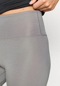 Harmaat legginsit, jotka on valmistettu sileästä, joustavasta kankaasta ja joissa on korkea vyötärökaistale. Niissä on litteät saumat ja tyylikäs, istuva muotoilu.