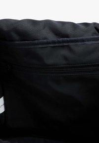 Interior de bolsa de tela negra con una textura suave, que cuenta con un bolsillo con cremallera y un diseño sin embellimientos. Compacta y funcional.