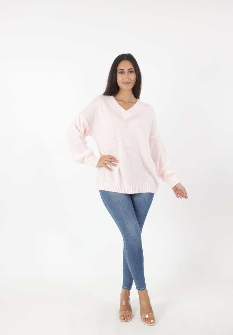 Helles rosa, übergroßes Strickpullover mit V-Ausschnitt und gerippten Bündchen, kombiniert mit blauen Skinny-Jeans und klaren Blockabsatzsandalen.