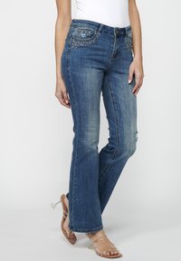 Vaqueros de denim azul con corte recto, con costuras decorativas y acentos de pedrería en los bolsillos delanteros. Acabado ligeramente desgastado.